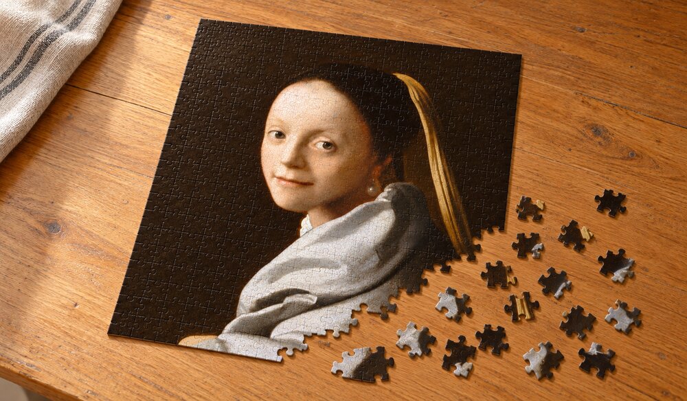 フェルメール「少女（Study of a Young Woman）」の組み立て途中を表したイメージ。銀灰色の布をまとう女性の縦長アートパズルが木のテーブルに置かれている